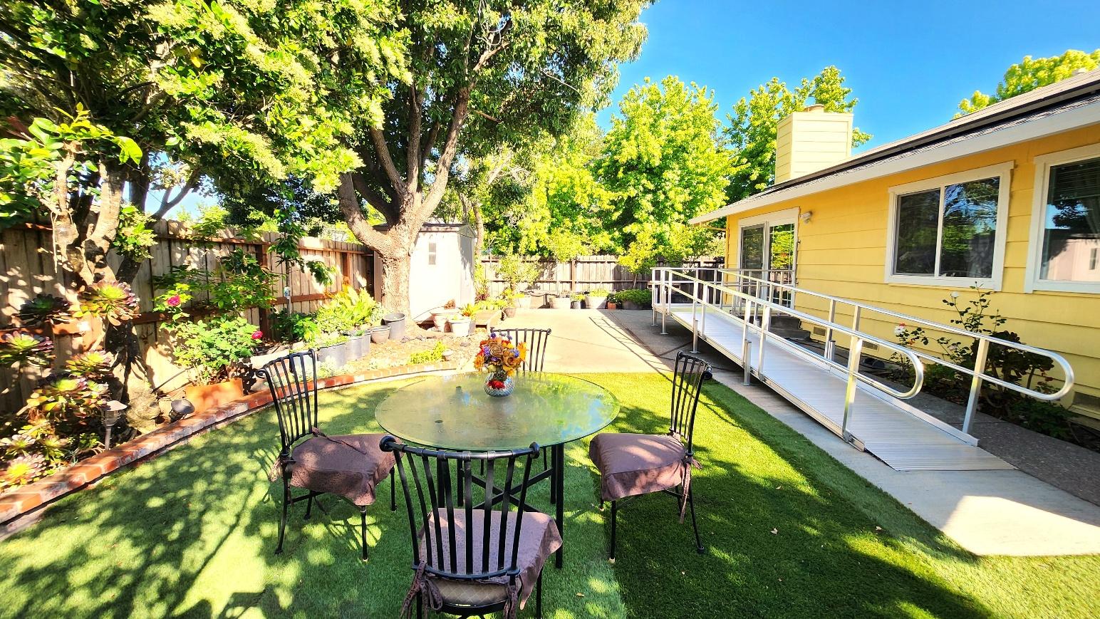 Backyard garden with a glass patio table, chairs, and mature shade trees
